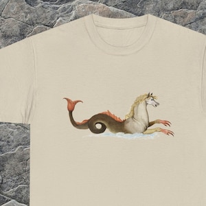 May include: A beige t-shirt with a graphic print of a mythical sea creature with a horse head and a fish tail. The creature is brown, gray, and orange.