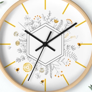 May include: A white round clock with a black hexagon in the center and black hands. The clock face has a floral design with yellow and orange flowers and bees. The clock has a wooden frame.