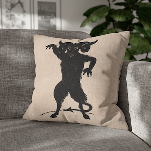 May include: A tan throw pillow with a black silhouette of a horned creature with a single eye. The creature is standing on its hind legs and has a tail.