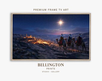 Op de afbeelding: Een ingelijste prent toont drie figuren op kamelen onder een sterrenhemel. Een heldere ster schijnt boven hen en leidt hun pad naar een stad die verlicht is met warme lichten. De tekst "PREMIUM FRAME TV ART" staat bovenaan.