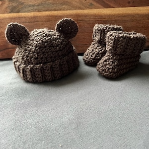 May include: A brown crocheted baby hat with bear ears and matching booties.
