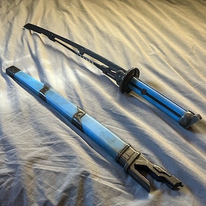 Può includere: Una spada in stile futuristico con un'impugnatura e un fodero azzurri e una lama nera. Il fodero è aperto, rivelando l'impugnatura della spada. La spada ha un design unico con dettagli intricati.