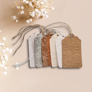 May include: Six gift tags with a floral design. The tags are in various colors, including silver, gold, and brown. Each tag has a hole at the top for string or ribbon.