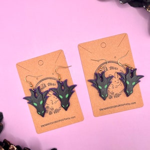 May include: Two pairs of black and green dragon head earrings on brown card stock with the text "ENCHANTEDIOKKIROOM.etsy.com".