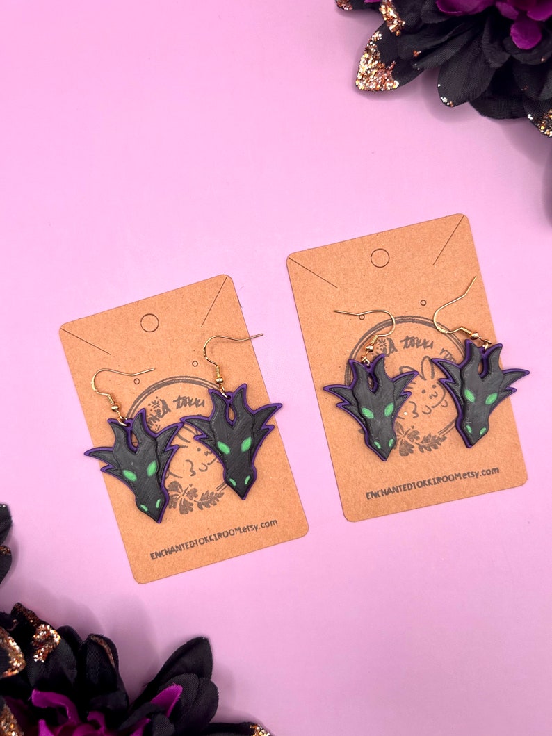 May include: Two pairs of black and green dragon head earrings on brown card stock with the text "ENCHANTEDIOKKIROOM.etsy.com".
