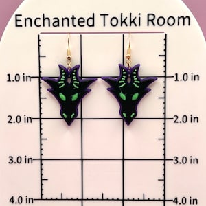May include: A pair of black and purple earrings with a green dragon design. The earrings are approximately 2 inches long.