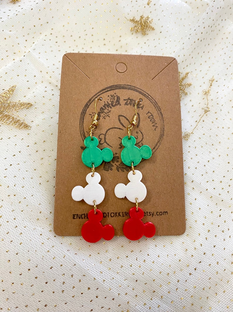 May include: Green, white and red Mickey Mouse-shaped dangle earrings. The earrings are made of polymer clay and have gold hooks.