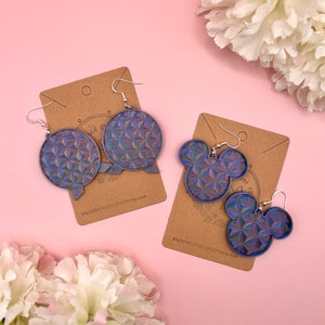 K&ouml;nnte beinhalten: Zwei Paar Ohrringe mit geometrischem Muster in Blau, Lila und Gold. Ein Paar ist kreisf&ouml;rmig, das andere hat die Form von Mickey Mouse. Beide Paare sind auf braunen Karten mit silbernen Ohrhaken abgebildet.