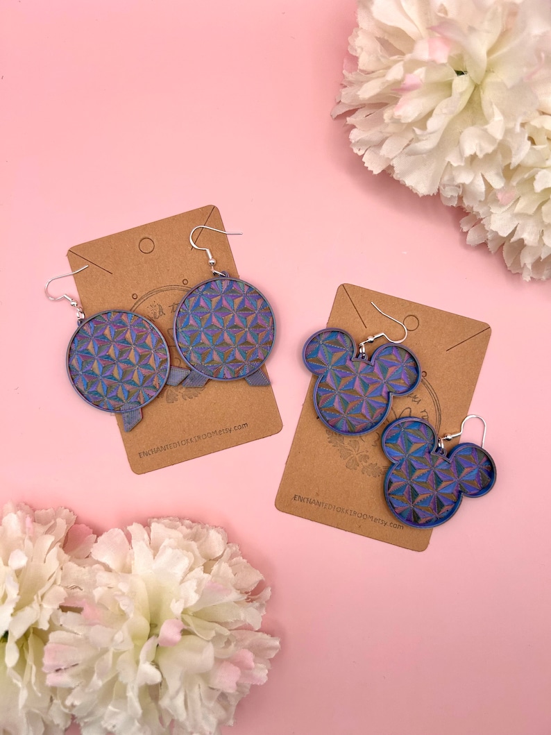 K&ouml;nnte beinhalten: Zwei Paar Ohrringe mit geometrischem Muster in Blau, Lila und Gold. Ein Paar ist kreisf&ouml;rmig, das andere hat die Form von Mickey Mouse. Beide Paare sind auf braunen Karten mit silbernen Ohrhaken abgebildet.