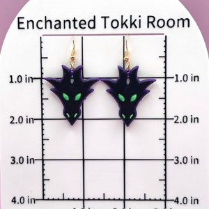 May include: A pair of purple and black dragon earrings with green eyes. The earrings are approximately 1.5 inches long and are hanging from gold hooks.