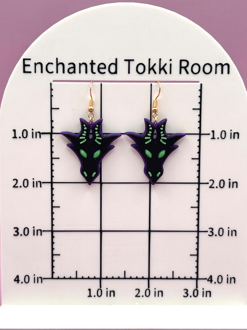 May include: A pair of black and green dragon earrings with gold hooks. The earrings are approximately 1 inch in length.