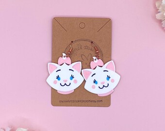 May include: A pair of white cat-shaped dangle earrings with pink bows and blue eyes. The earrings are on a brown card with the text "ENCHANTEDTOKKIROOMEtsy.com".