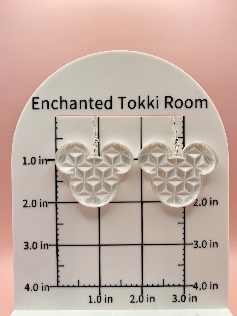 K&ouml;nnte beinhalten: Klare Ohrringe in Form eines Mickey Mouse-Kopfes aus Acryl mit einem geometrischen Muster. Die Ohrringe werden auf einem wei&szlig;en St&auml;nder mit dem Text "Enchanted Tokki Room" pr&auml;sentiert. Die Ohrringe sind etwa 5 cm hoch.