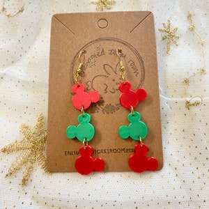 May include: Red and green Mickey Mouse-shaped dangle earrings with gold hooks. The earrings are on a brown card with the text "Enchanted Room Etsy".