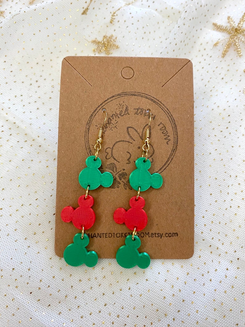 May include: A pair of dangle earrings featuring three green and two red Mickey Mouse head charms. The earrings are on a brown card with the text "Haunted10kroom.etsy.com".