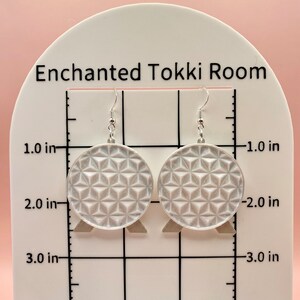 K&ouml;nnte beinhalten: Ein Paar silberfarbene H&auml;ngeohrringe. Jeder Ohrring ist ein Kreis mit einem geometrischen Muster. Die Ohrringe haben einen Durchmesser von etwa 5 cm und h&auml;ngen an silbernen Haken. Der Text "Enchanted Tokki Room" ist im Hintergrund sichtbar.