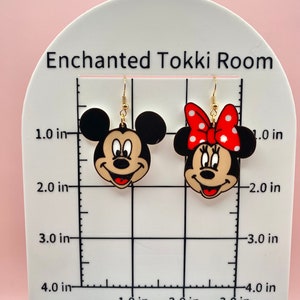 May include: A pair of gold-tone earrings featuring cartoon images of Mickey and Minnie Mouse. The earrings are approximately 1 inch in diameter.