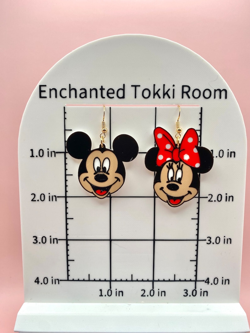 May include: A pair of gold-tone earrings featuring cartoon images of Mickey and Minnie Mouse. The earrings are approximately 1 inch in diameter.