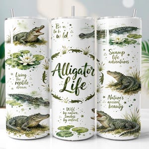 May include: Three white cylindrical tumblers with metal straws, featuring watercolour illustrations of alligators in swamp settings, green lily pads, and text including Alligator Life, Born to be wild, Living the reptile dream, and Swamp life adventures.