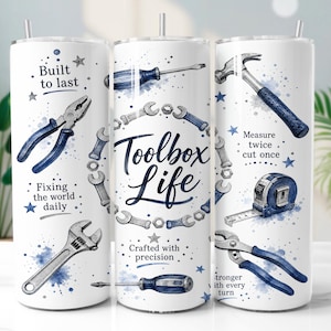 May include: Three white cylindrical tumblers with metal straws, featuring blue watercolor tool illustrations including pliers, a hammer, a tape measure, and wrenches. Text includes "Built to last," "Toolbox Life," "Measure twice cut once," and "Crafted with precision."