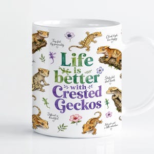 Pode incluir: Uma caneca de cerâmica branca com ilustrações em aguarela de geckos-de-crista em ramos, pequenas flores e folhas verdes. O texto diz Life is better with Crested Geckos, juntamente com frases como Tiny feet, big personality e Sticky feet, steal hearts.
