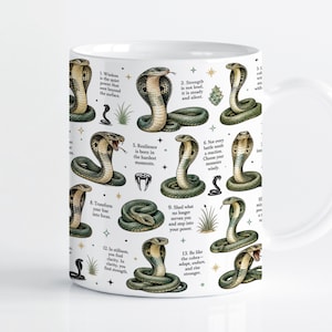 Op de afbeelding: Een witte keramische mok met een herhalend patroon van groene en bruine cobra-illustraties. Het ontwerp bevat kleine gouden sterren, groene planttakjes en genummerde tekstpassages met motiverende citaten over kracht en veerkracht.
