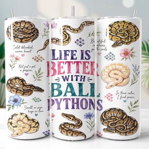 May include: A white cylindrical tumbler featuring illustrations of ball pythons in various coiled positions, colorful floral accents, and the text "LIFE IS BETTER WITH BALL PYTHONS" in large, bold, multi-colored lettering, topped with a clear straw.