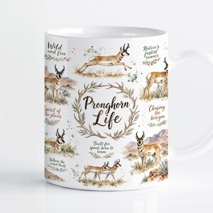 May include: A white ceramic mug featuring a wrap-around watercolor illustration of pronghorn antelopes in various poses. The central text reads "Pronghorn Life" surrounded by a wreath, with phrases like "Wild and free" and "Nature's fastest runner" printed in a script font.