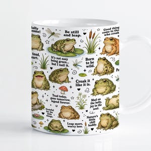 Pode incluir: Uma caneca de cerâmica branca com um padrão repetitivo de sapos verdes e castanhos, libélulas, cogumelos e taboas. O design inclui frases em preto como Be still and leap, Born to be wild e Croak it like it is, intercaladas com pequenas estrelas.
