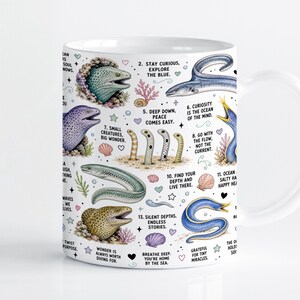 Pode incluir: Uma caneca de cerâmica branca com uma ilustração colorida de várias enguias, incluindo moreias e enguias-de-jardim, intercaladas com pequenas conchas, corais e estrelas. O design inclui frases inspiradoras numeradas em fonte preta.