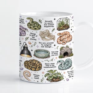 Könnte beinhalten: Ein weißer Keramikbecher mit farbenfrohen Illustrationen verschiedener Schlangen, einem Terrarium, einer Wärmelampe, einer Wasserschale und einer Felshöhle. Das Design enthält inspirierende Texte wie Growth is quiet, but always happening.