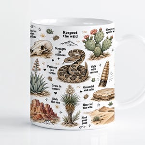 Puede incluir: Una taza de cerámica blanca con una ilustración de temática desértica que incluye una serpiente de cascabel, un cactus, un cráneo animal, formaciones rocosas y dunas. El diseño incluye frases como Respect the wild, Strength in stillness y Patience is a virtue.
