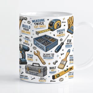 Könnte beinhalten: Ein weißer Keramikbecher mit einem bunten Muster aus Bauwerkzeugen wie Maßband, Hammer, Bohrmaschine, Schraubenschlüssel und Werkzeugkasten, durchsetzt mit motivierenden Sprüchen wie Measure Twice Cut Once und Build Your Dreams.