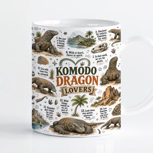 Pode incluir: Uma caneca de cerâmica branca com uma estampa gráfica detalhada de dragões de Komodo em várias poses, paisagens tropicais e legendas numeradas. O texto central diz KOMODO DRAGON LOVERS em letras de cor verde-escura e laranja.