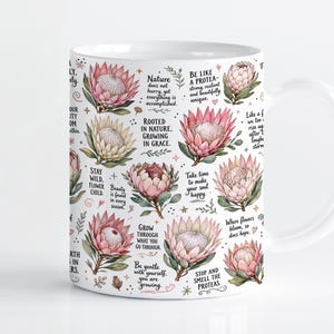 Pode incluir: Uma caneca de cerâmica branca com um padrão repetitivo de flores protea cor-de-rosa e creme, folhas verdes e pequenas estrelas. O design inclui textos inspiradores como Be like a protea, Rooted in nature e Grow through what you go through.