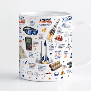 Könnte beinhalten: Ein weißer Keramikbecher mit einem farbenfrohen Grafikdruck zum Thema Weltraum. Das Design zeigt Illustrationen von Raketen, einem Fallschirm, einer Schutzbrille und einer Fernbedienung, begleitet von Texten wie Engine Ignition und Clear Skies Ahead.