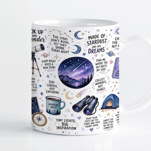Pode incluir: Uma caneca de cerâmica branca com um padrão de temática celestial, apresentando ilustrações de um telescópio, binóculos, uma tenda, uma bússola e um céu estrelado. O design inclui textos inspiradores como Made of Stardust and Big Dreams.