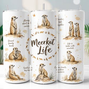 Puede incluir: Un vaso cilíndrico blanco con pajita de metal, que presenta ilustraciones en acuarela de suricatas en varias posturas. El texto dice Meerkat Life, Always alert and curious, Desert family bonds, Standing tall together, Life is better with meerkats, Small paws, big impact y Curious hearts, boundless adventures.