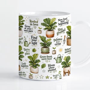 May include: A white ceramic mug featuring a repeating pattern of potted fiddle leaf fig plants, green watering cans, and gardening tools. The design includes inspirational text such as Rooted in love, Grow at your own pace, Find your light, and Bloom where planted.