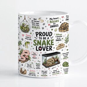 Puede incluir: Una taza de cerámica blanca con un estampado gráfico colorido de varias serpientes, terrarios y citas sobre serpientes, incluido el texto central Proud to be a snake lover. El diseño incluye ilustraciones de serpientes en diferentes colores y hábitats.