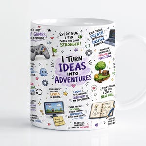 May include: A white ceramic mug featuring colourful illustrations and text related to game development. The central text reads I TURN IDEAS INTO ADVENTURES, surrounded by icons of a game controller, a computer, a treasure chest, and a notebook.