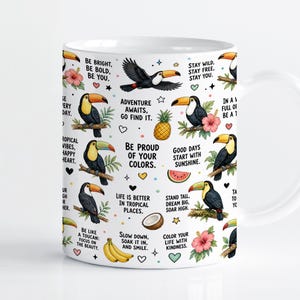 Könnte beinhalten: Ein weißer Keramikbecher mit einem wiederkehrenden Muster aus Tukanen, Ananas, Bananen, Kokosnüssen, Wassermelonenscheiben und Hibiskusblüten. Das Design enthält inspirierende Texte wie Be Bright, Be Bold, Be You und Adventure Awaits, Go Find It.