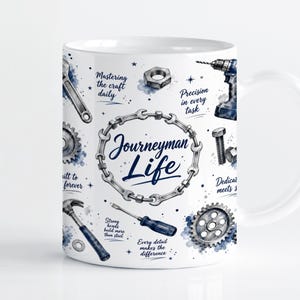 Könnte beinhalten: Ein weißer Keramikbecher mit einer blau-grauen Illustration verschiedener Werkzeuge wie Schraubenschlüssel, Hammer, Schraubendreher, Bohrer, Zahnräder und Muttern. Der Text "Journeyman Life" ist in einem Kreis aus Kettengliedern zentriert.