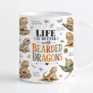 May include: A white ceramic mug featuring multiple watercolour illustrations of bearded dragons in various poses. The text reads: Life is better with bearded dragons, along with small floral accents, insects, and phrases like Tiny dinosaur, major personality.