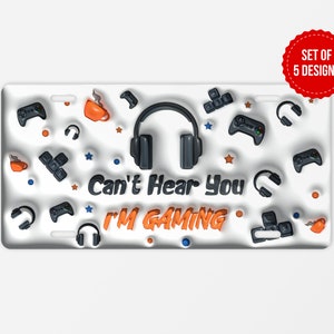 Puede incluir: Placa de matrícula blanca con un diseño negro y naranja. El diseño presenta unos auriculares, mandos de juego y el texto "Can't Hear You I'm Gaming".