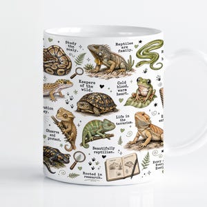 Könnte beinhalten: Ein weißer Keramikbecher mit einer farbenfrohen Illustration verschiedener Reptilien und Amphibien, darunter eine Schlange, eine Schildkröte, eine Eidechse und ein Frosch, sowie kleine Symbole wie Lupen und ein offenes Feldbuch mit Text.