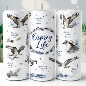 Puede incluir: Un vaso cilíndrico blanco con ilustraciones en acuarela de águilas pescadoras en vuelo y posadas, ramas de pino y texto azul que incluye "Osprey Life", "Soaring with the tide", "Born to ride the wind" y "Nature's skilled fisher".