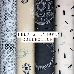 May include: Four rolls of fabric from the Luna & Laurel Collection. The rolls feature various patterns, including geometric shapes, celestial designs, and abstract lines. Colors include black, white, and beige. The text "LUNA & LAUREL COLLECTION" is displayed.