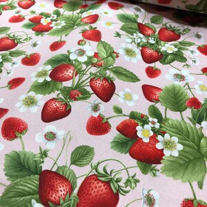 May include: Pink fabric with a repeating pattern of red strawberries and white flowers. The strawberries are depicted with green leaves and stems.