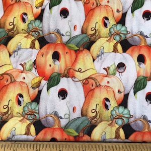 Puede incluir: Una tela impresa con un patrón de calabazas blancas, naranjas y amarillas con pequeños ratones asomándose por los agujeros de las calabazas. La tela está sobre un fondo negro y tiene una regla y una etiqueta para Blue Snowman Fabrics.